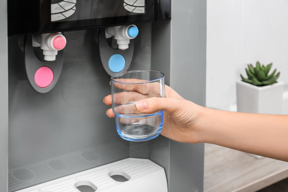 A person filling a glass of water from a water dispenser.