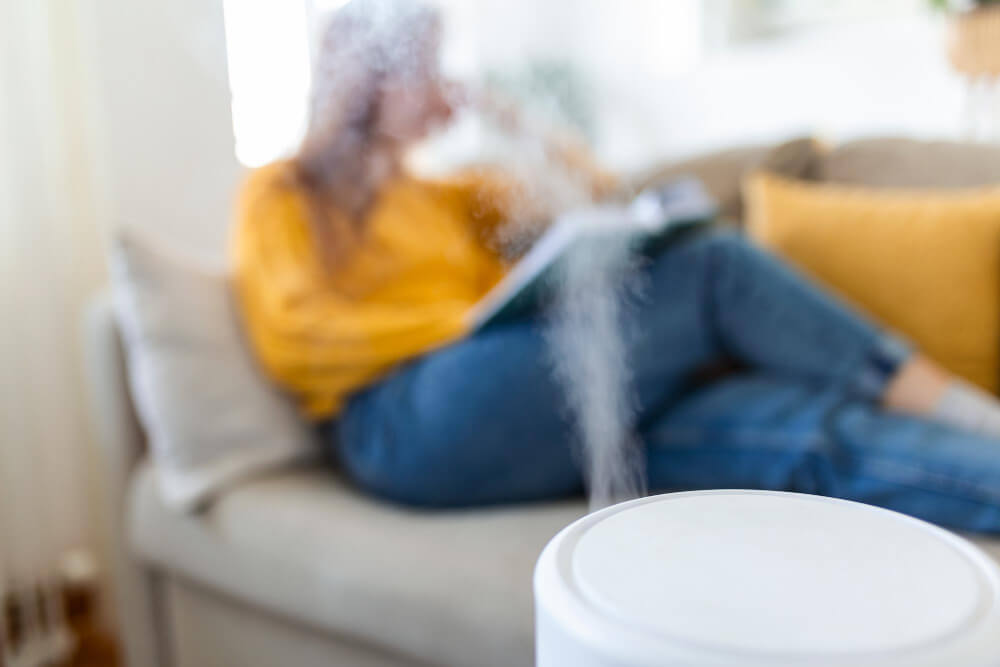 A woman sitting on a couch with a humidifier.
