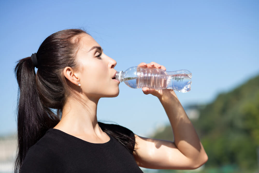 A young woman drinking water from a bottle.