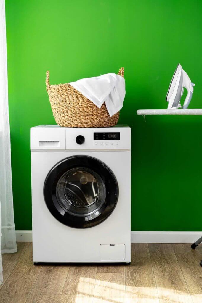 A washing machine sits in front of a green wall.