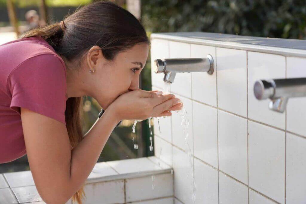 A person drinks water from a tiled outdoor faucet by cupping their hands.