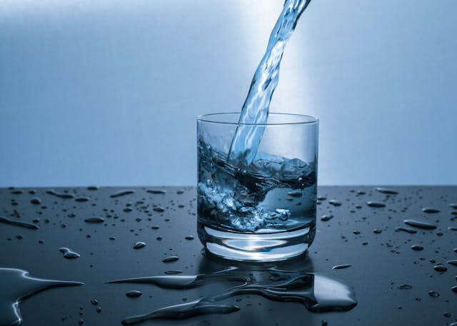 Water being poured into a clear glass, with droplets scattered on a reflective surface.