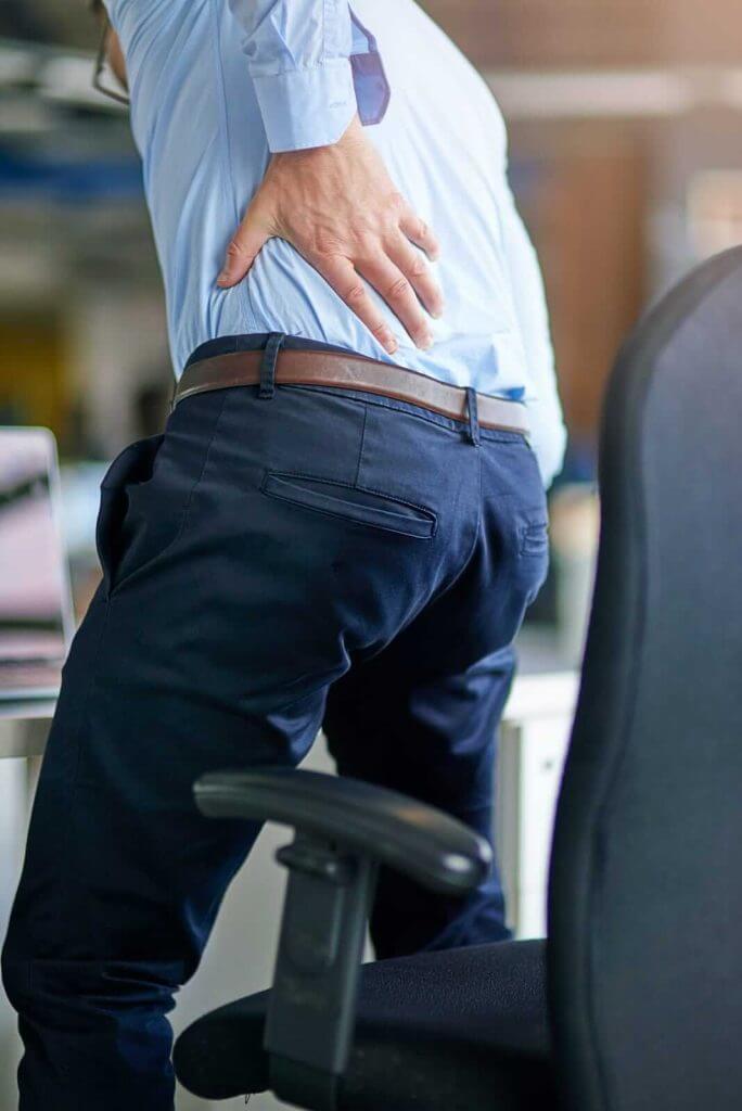 Person in office attire standing up from a chair, holding their lower back with a pained expression.