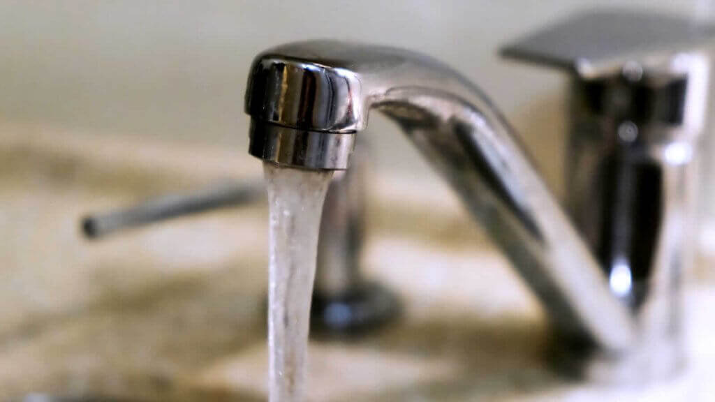 Close-up of a metallic faucet with water flowing into a beige sink.