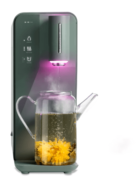A kitchen appliance dispensing hot water with a purple light into a glass teapot containing yellow blooming tea flowers.